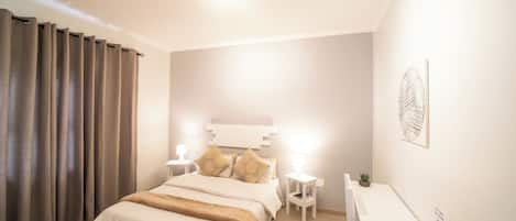 Ein Hotelzimmer mit Bett, Nachttischen, Schreibtisch, Stuhl, einer kleinen Pflanze und einem Wandbild.