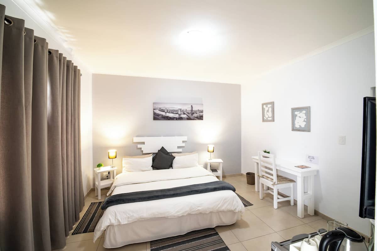 Hotellihuone, jossa on sänky, yöpöydät, työpöytä ja tuoli.