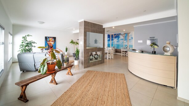 A modern living room with a sofa, a bench, and potted plants. There is a glass coffee table and a dining area with chairs. - Bella Luna B&B (Walvis Bay)