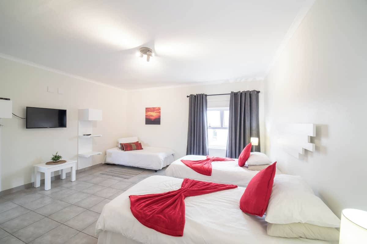 Hotellihuone, jossa on kaksi sänkyä, televisio, pieni pöytä ja ikkuna, jossa on verhot.