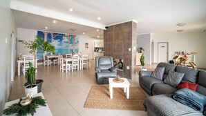 A spacious living area with a grey sofa, a white coffee table, and a dining area with white chairs and a table. - Bella Luna B&B (Walvis Bay)