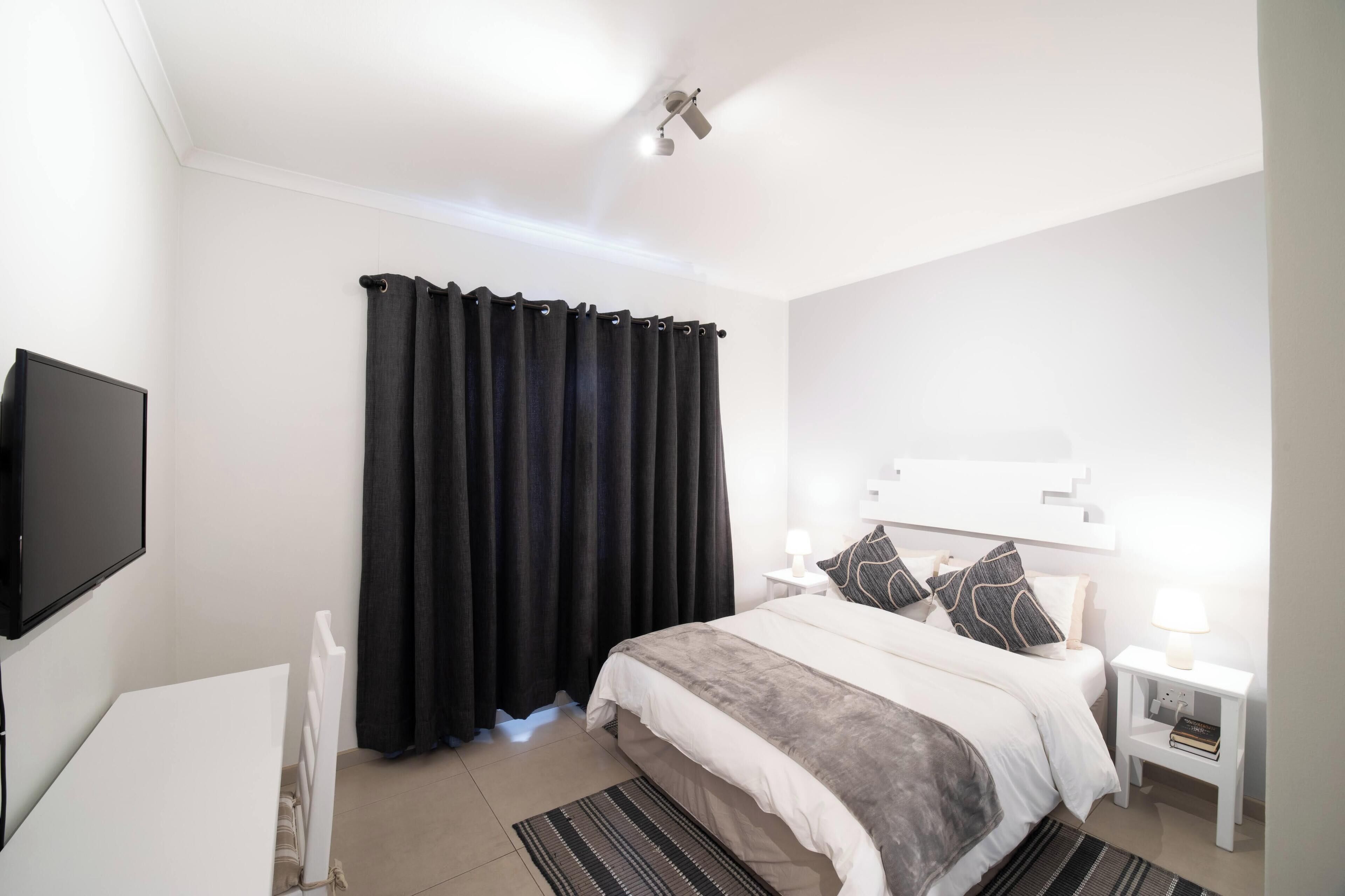 A bedroom with a bed, bedside tables, a TV, and a ceiling fan.