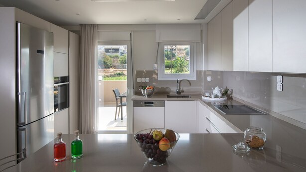 A modern kitchen with stainless steel appliances, a bowl of fruit on the counter, and a view of the outdoors. - Gras Houses Agia Pelagia (Malevizi)