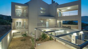 A multi-story modern house with multiple balconies, a covered outdoor area, and a well-lit interior. - Gras Houses Agia Pelagia (Malevizi)
