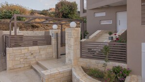 A modern building with a stone pathway leading to a gated entrance, a small garden area, and a staircase to the upper level. - Gras Houses Agia Pelagia (Malevizi)