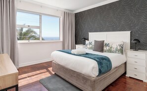 Une chambre à coucher avec un grand lit, une table de chevet, un bureau et une fenêtre avec des rideaux.
