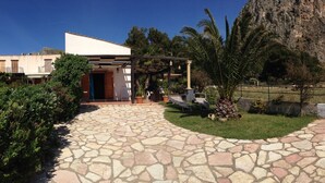 A stone-paved courtyard with a pergola, a mountain backdrop, and a building with a white facade.