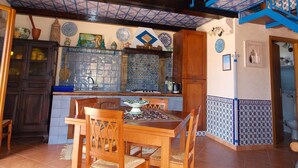 A spacious kitchen with a dining area, featuring a wooden table and chairs, a blue staircase, and decorative tiles.
