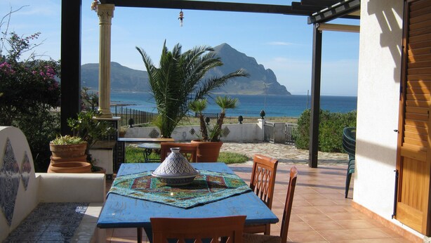 A patio with a table and chairs, a decorative bowl, and a view of the sea and mountains.