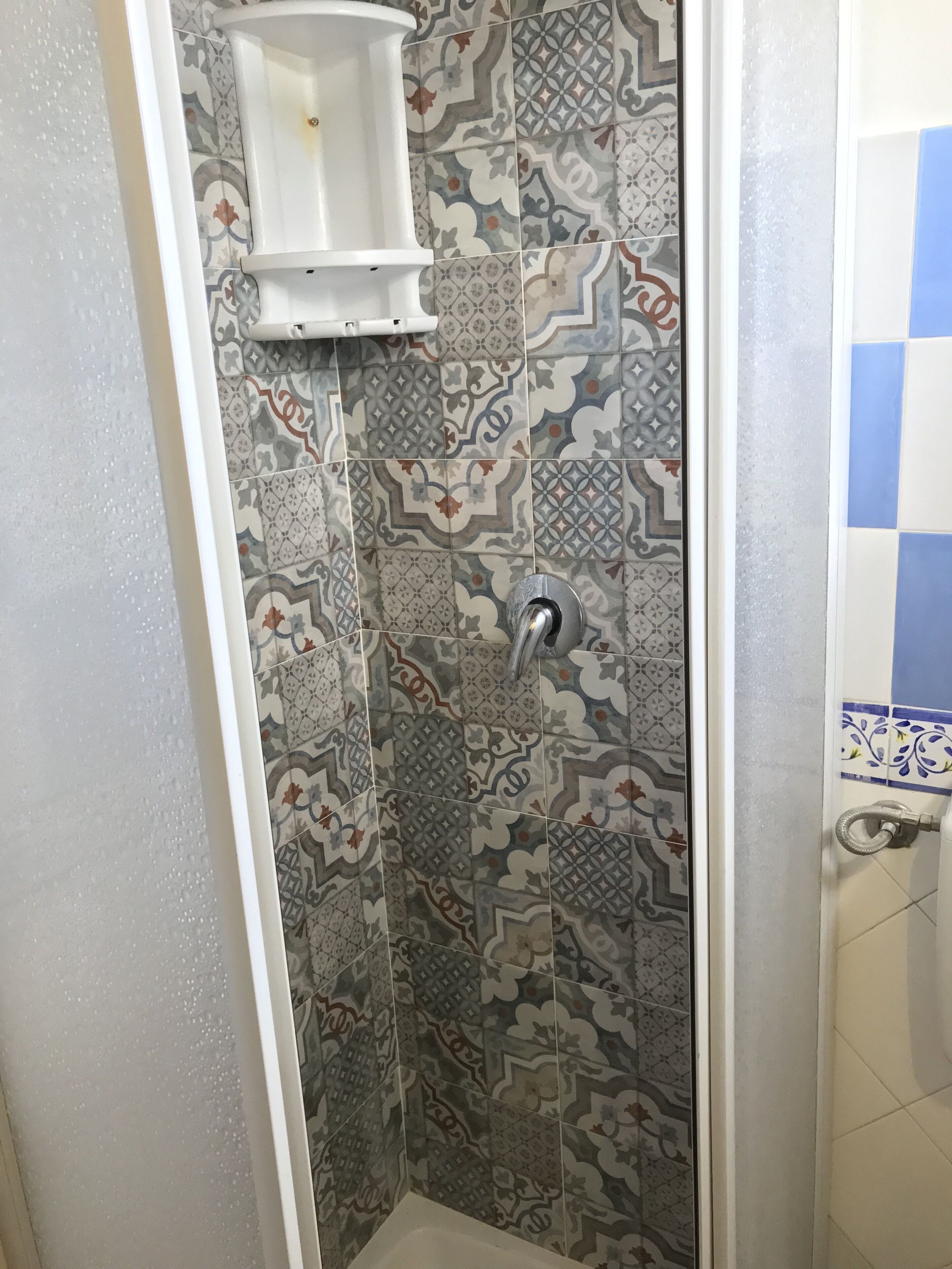 Uma área de chuveiro com azulejos estampados e uma pia branca.