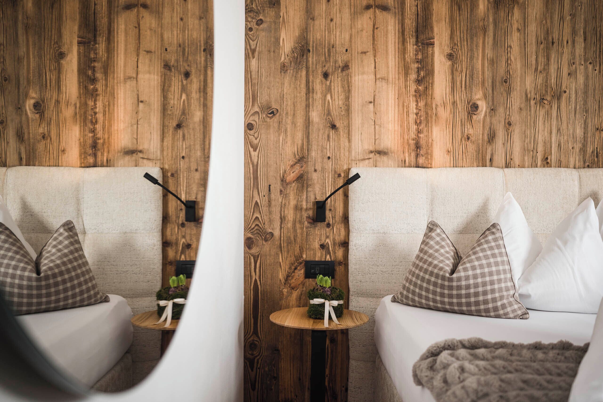 Une pièce avec un mur en bois, un canapé agrémenté de coussins à carreaux, une petite table ronde avec une plante et une couverture posée sur le canapé.