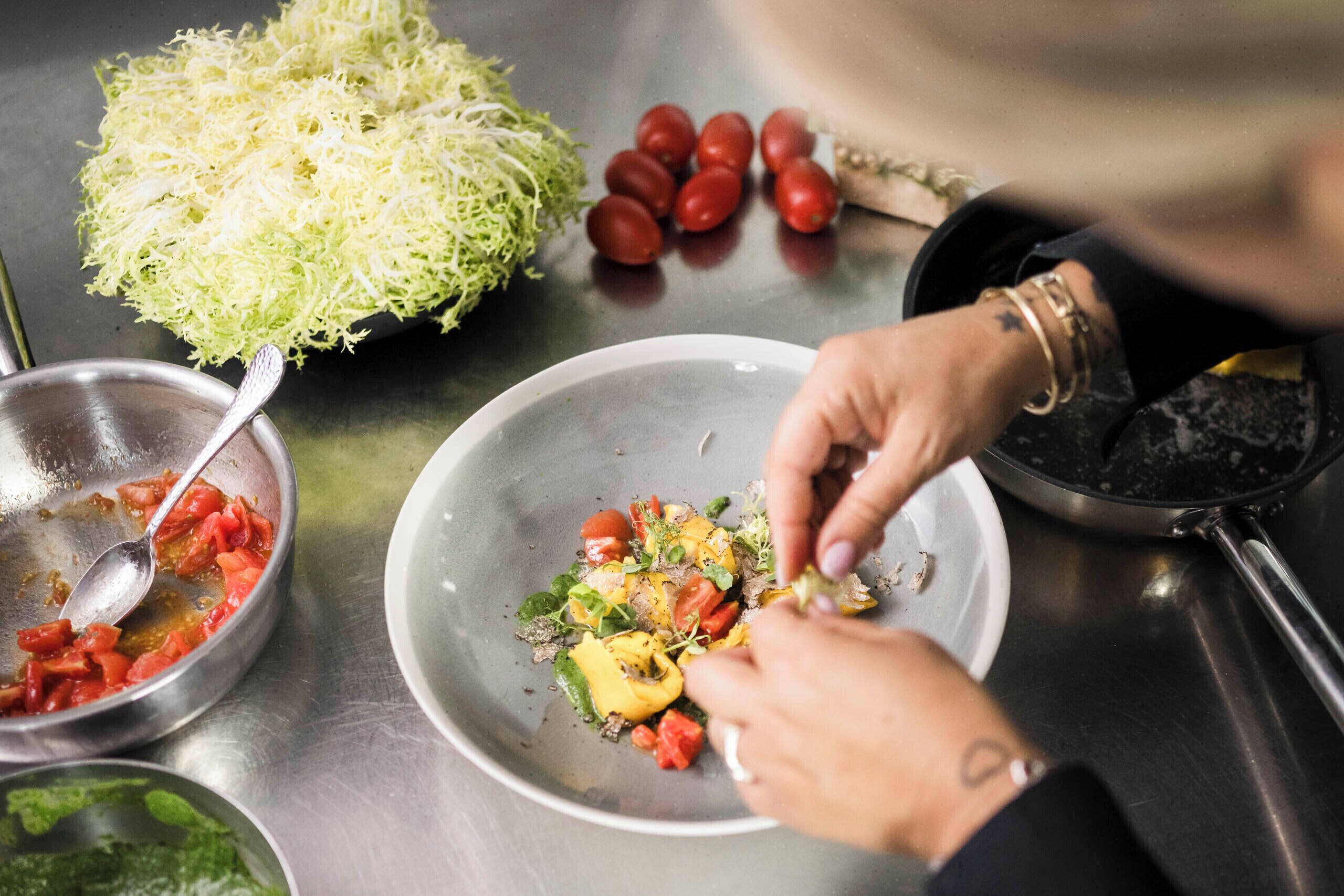 A person preparing a dish with vegetables and a bowl of shredded cabbage.