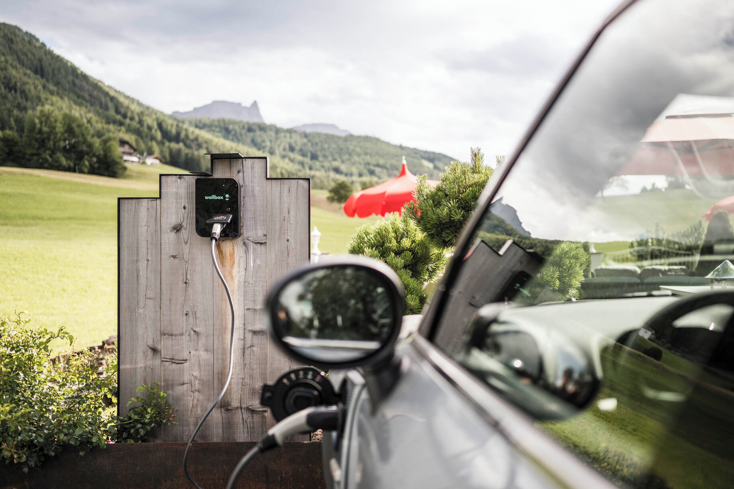 A car parked at a charging station with a view of a green landscape and mountains in the background.