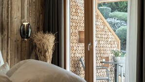 A bedroom with a bed, a wooden wall, a hanging light fixture, and a view of an outdoor area with a table and chairs. - Alpine Boutique Villa Gabriela (Castelrotto)