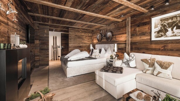 A cozy room with a wooden ceiling, a bed, a sofa, and a coffee table. There are skis leaning against the wall and a framed picture above the sofa. - Alpine Boutique Villa Gabriela (Castelrotto)