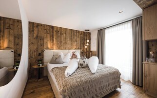 Un dormitorio moderno con una pared de acento de madera, una cama grande con muchos almohadones, una mesita de noche y otra mesilla.