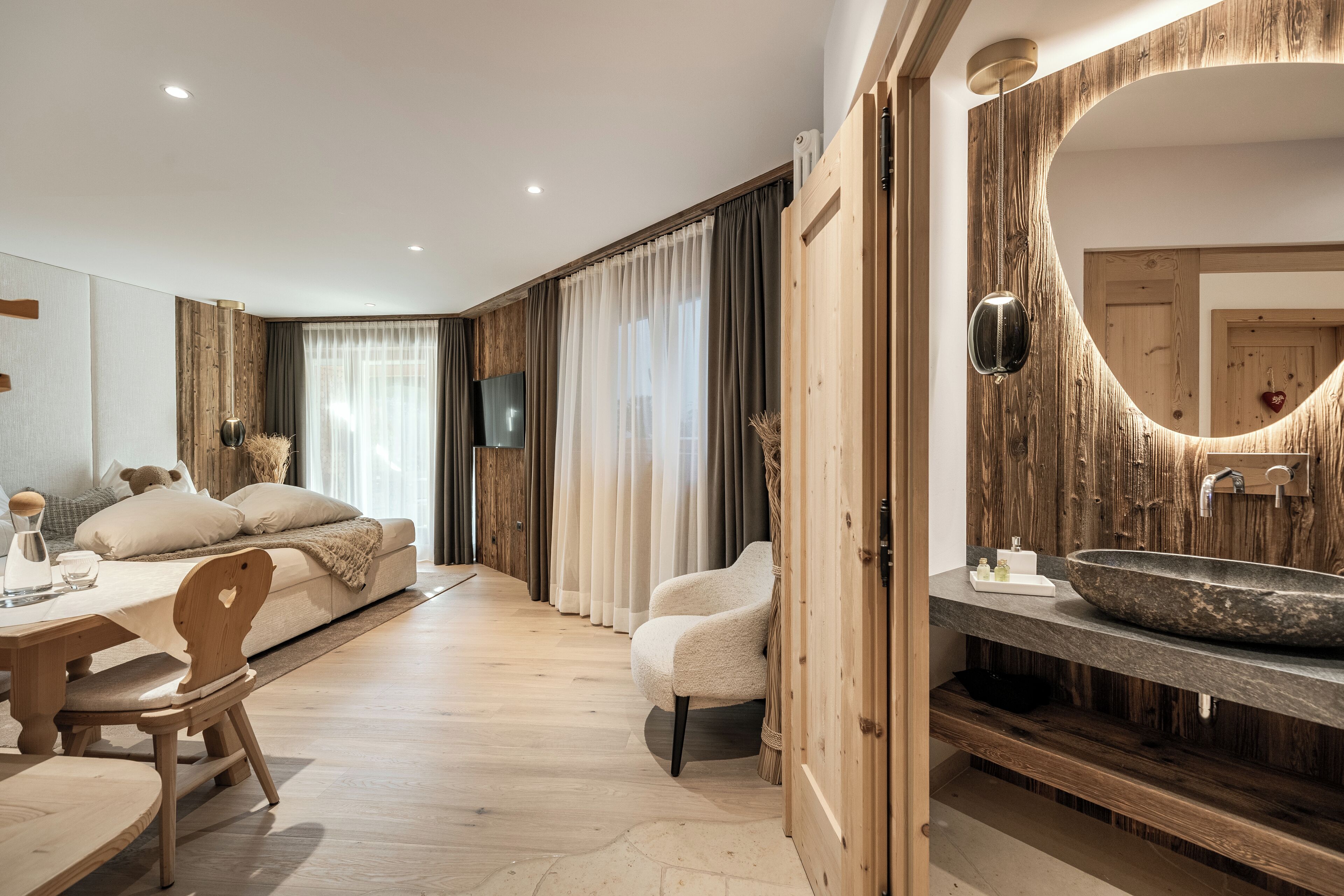 A modern bedroom with a wooden floor, a large bed with a headboard, a bedside table, a chair, and a large mirror.