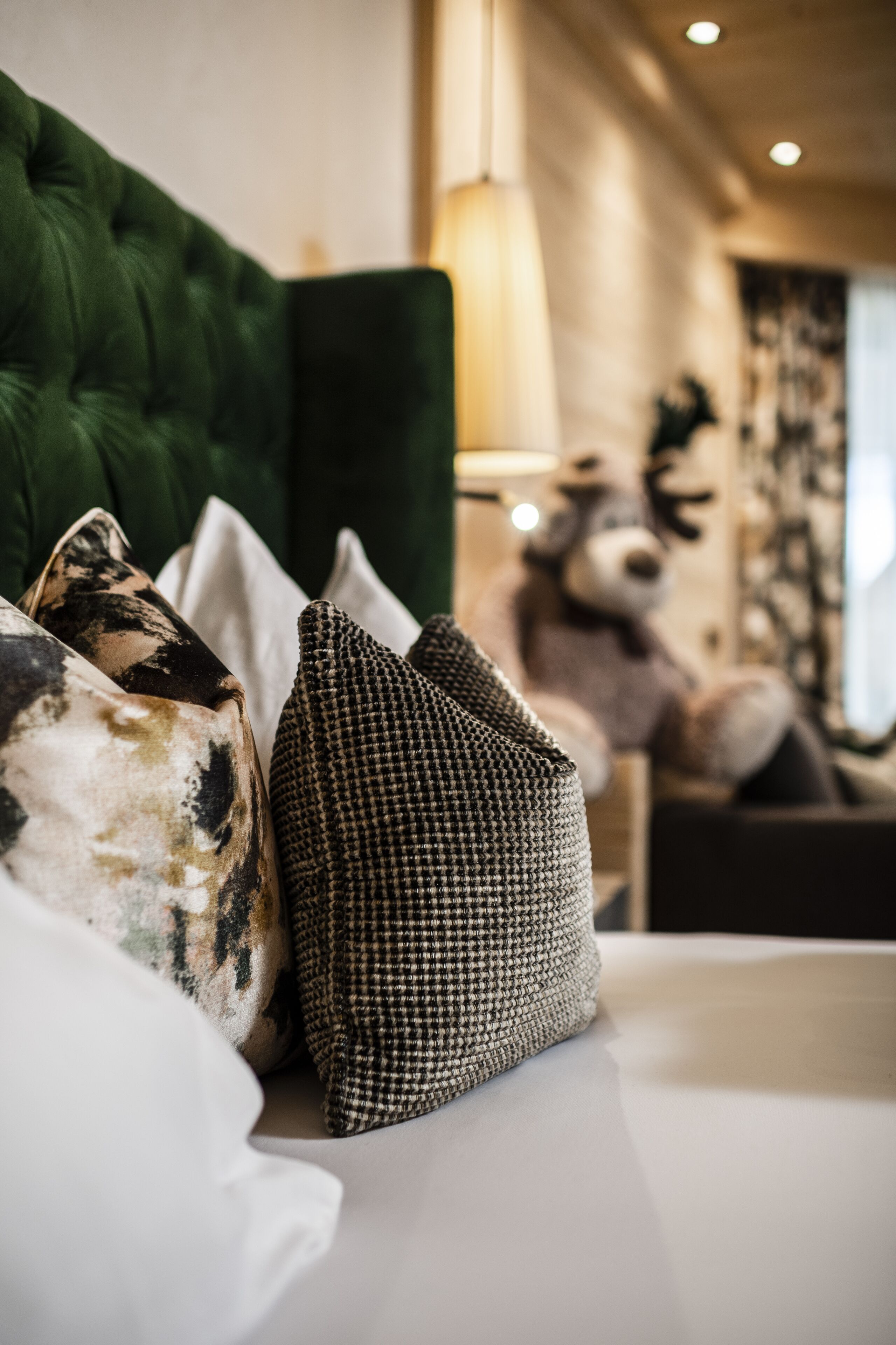A bed with multiple pillows, a green upholstered headboard, and a lamp in the background.