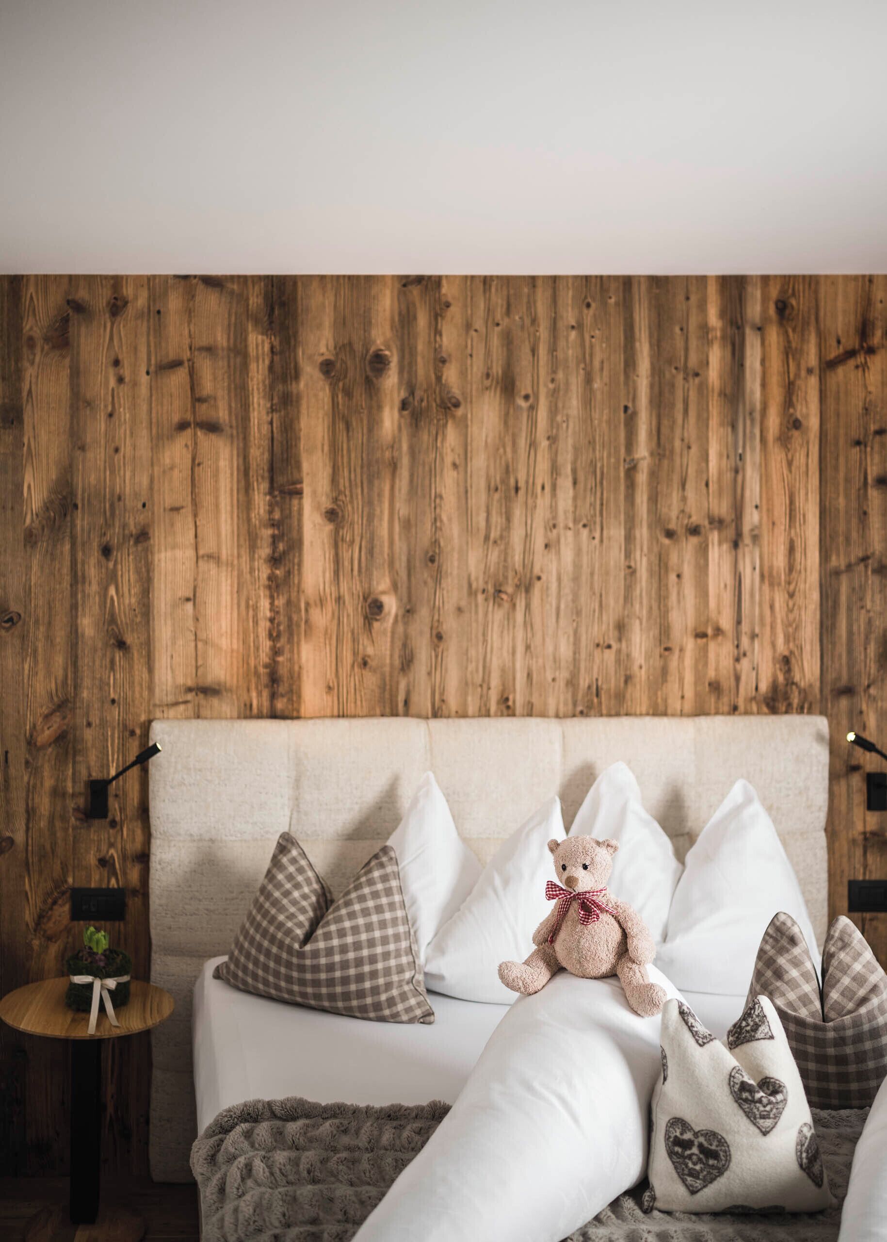 Une pièce chaleureuse avec un mur en bois, un canapé agrémenté de coussins à carreaux, un ours en peluche et une petite table ronde sur laquelle est posée une plante.