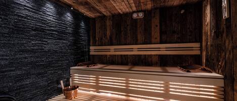 Una sauna con paredes y bancos de madera, una pared de piedra y un techo de madera.
