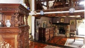 Una habitación tradicional con vigas de madera, chimenea y un aparador de madera lleno de objetos.