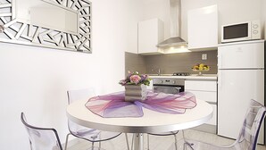 Eine moderne Küche mit weißen Schränken, einer Mikrowelle und einem Kühlschrank. Es ist ein runder Tisch mit Stühlen und eine Vase mit Blumen vorhanden.