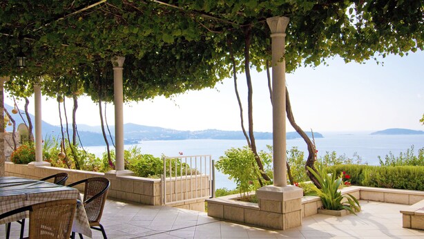 Eine Außenpatio mit Meerblick, ausgestattet mit einem Tisch, Stühlen, Pflanzgefäßen und einer Pergola.