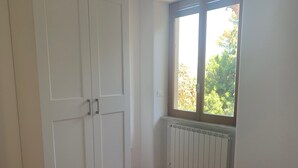 A room with a large wardrobe, a radiator, and a window with a view of trees. - Casa del sole, breathtaking view of the Pontine islands and the Circeo (Sperlonga)