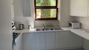 A modern kitchen with white cabinets, a stainless steel sink, a microwave, and a window with a view of greenery. - Casa del sole, breathtaking view of the Pontine islands and the Circeo (Sperlonga)