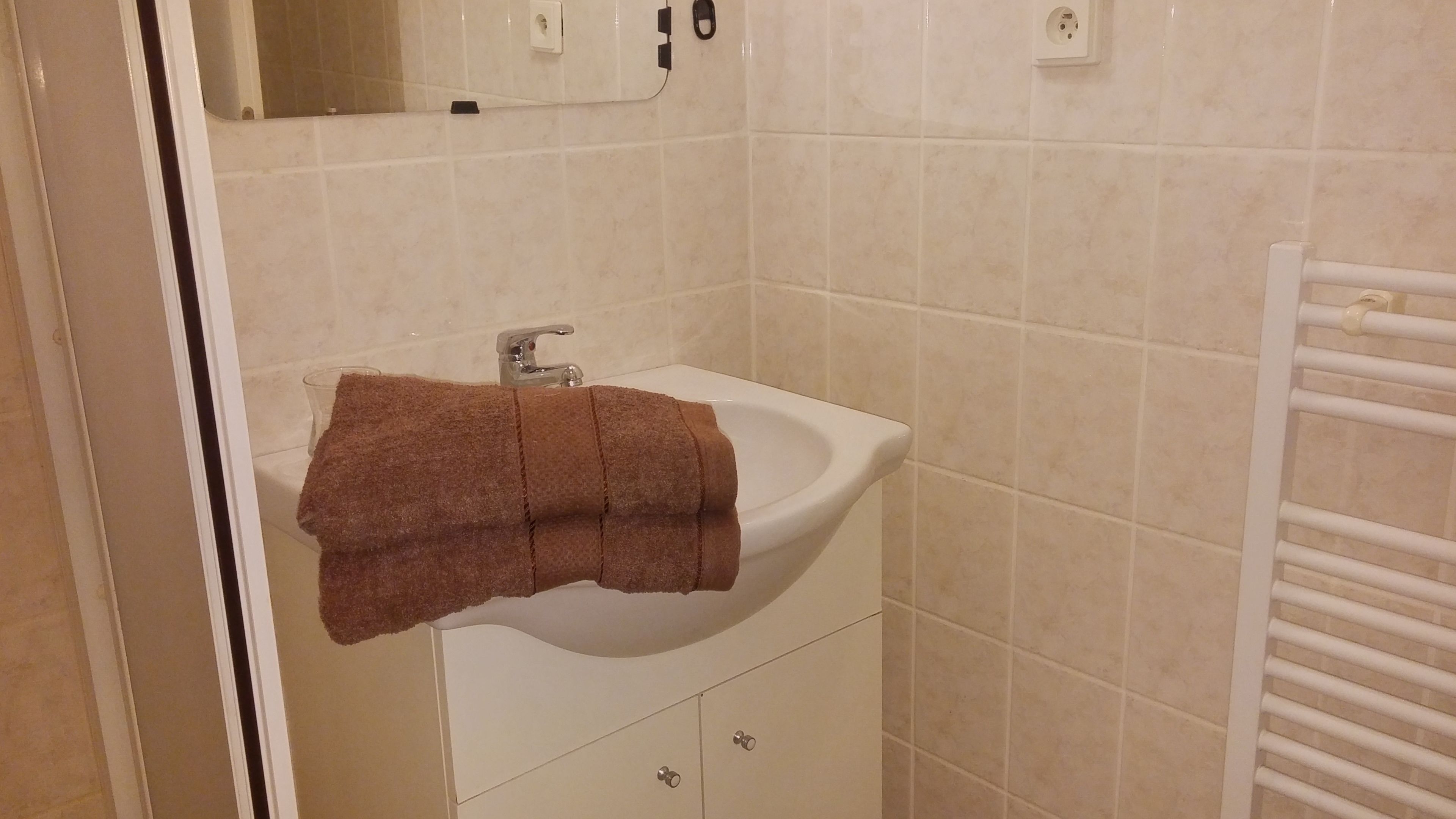 A bathroom with a white sink, a mirror above it, and a towel hanging on the wall.