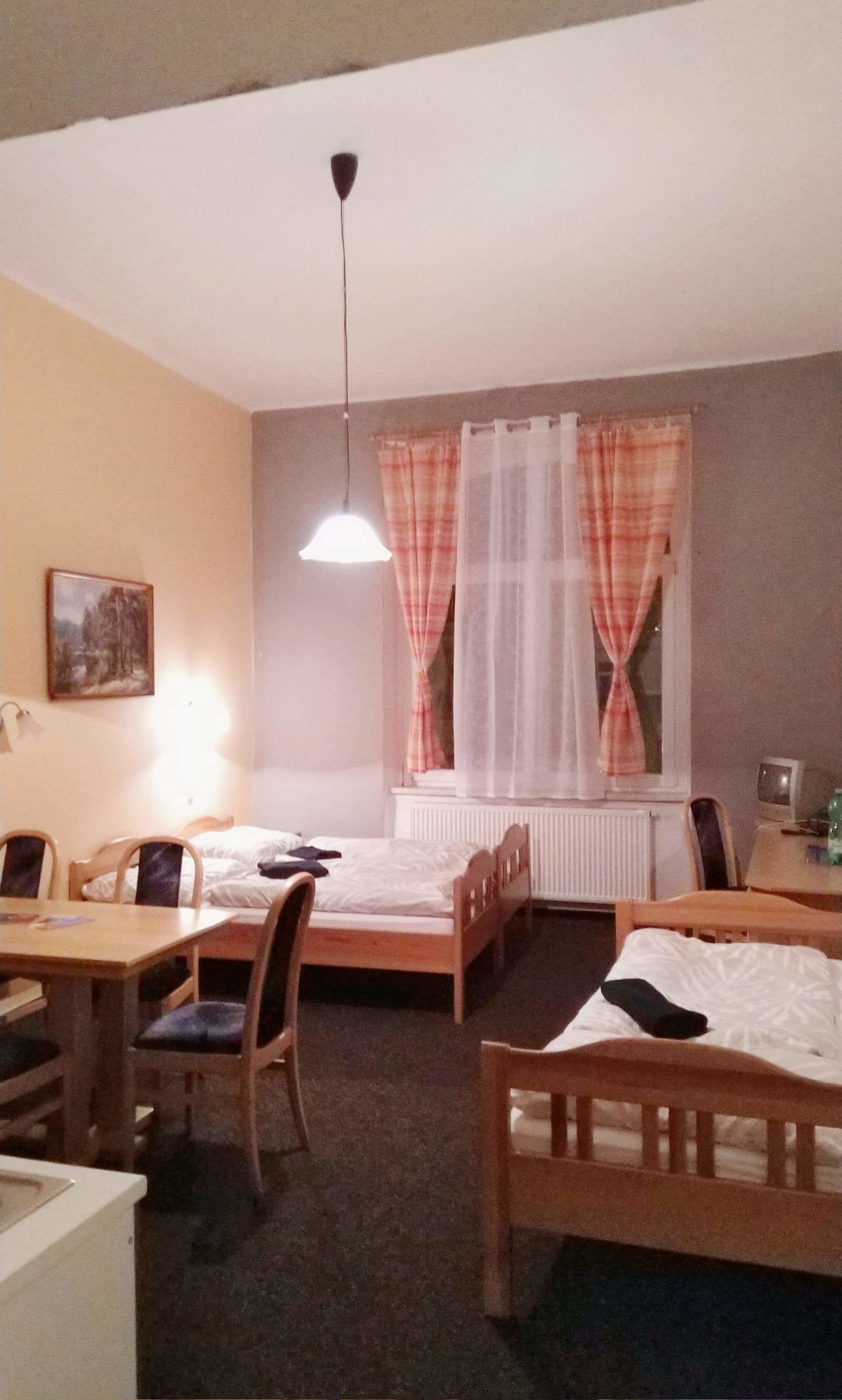 A small, cozy room with two single beds, a desk with a chair, a radiator, and a window with sheer curtains.