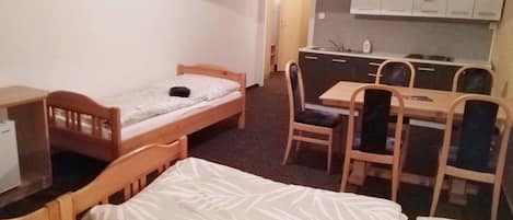 A small, compact room with a single bed, a desk, a chair, and a kitchenette area.