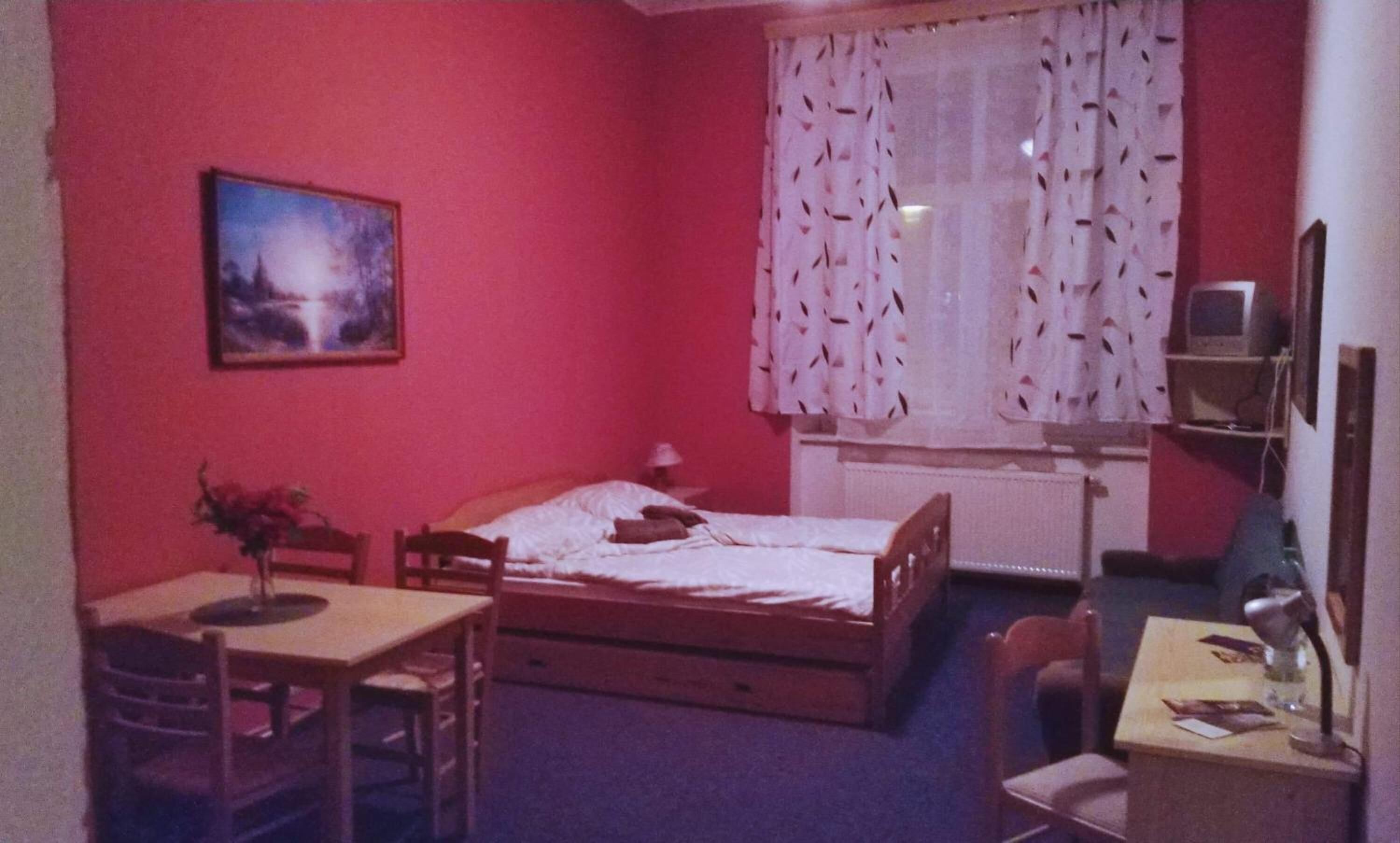 Een kleine kamer met rode wanden, een enkel bed, een bureau en een stoel.