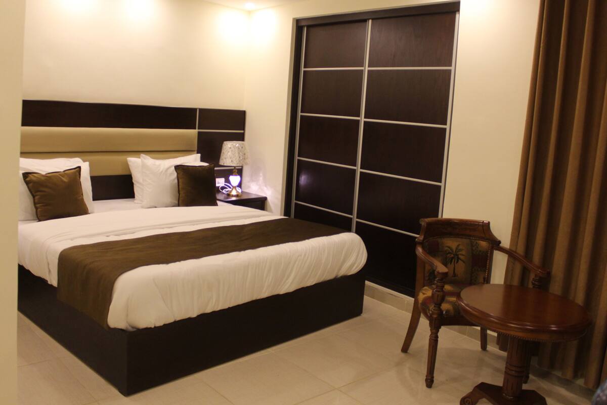 A neatly made bed with a headboard, a bedside table with a lamp, and a chair.