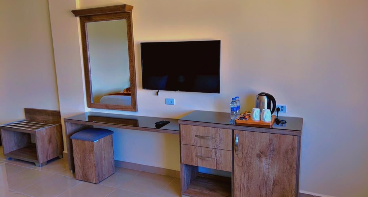Une chambre dotée d’une coiffeuse en bois, d’un grand miroir, d’un téléviseur à écran plat et d’une petite table sur laquelle se trouvent une bouilloire et des tasses.