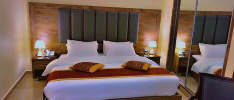 A hotel room with a large bed, two bedside tables with lamps, a mirror, and a wooden headboard.