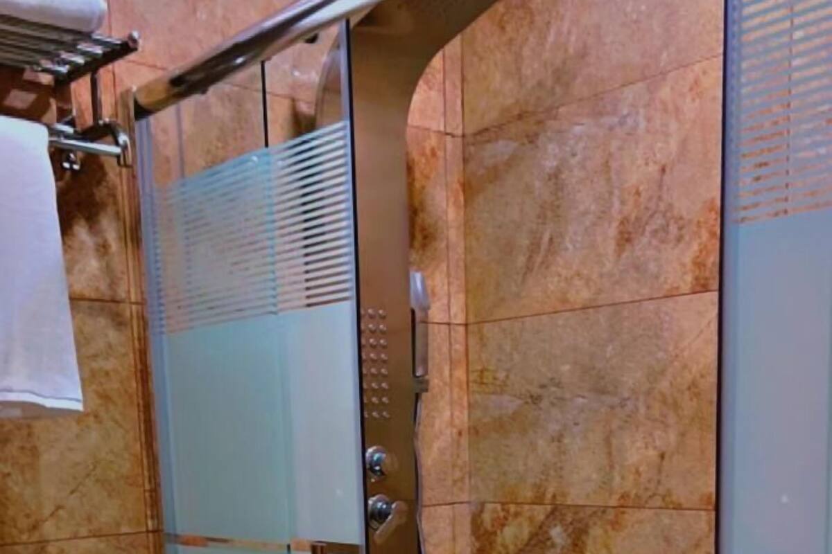 A glass-enclosed shower stall with a marble floor, a white toilet, and a towel rack.