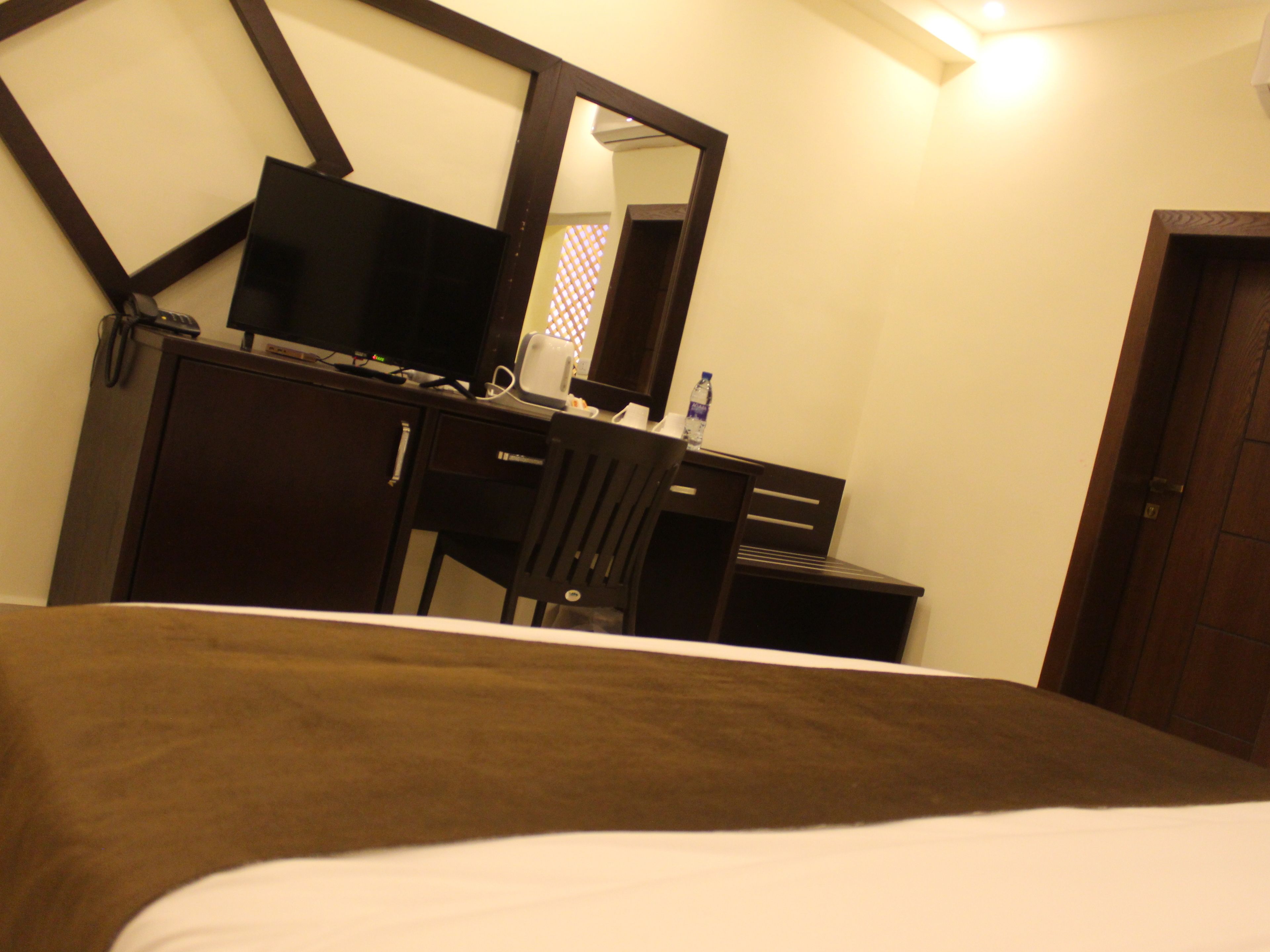 Habitación de hotel con cama, escritorio con computadora, silla, espejo y puerta.