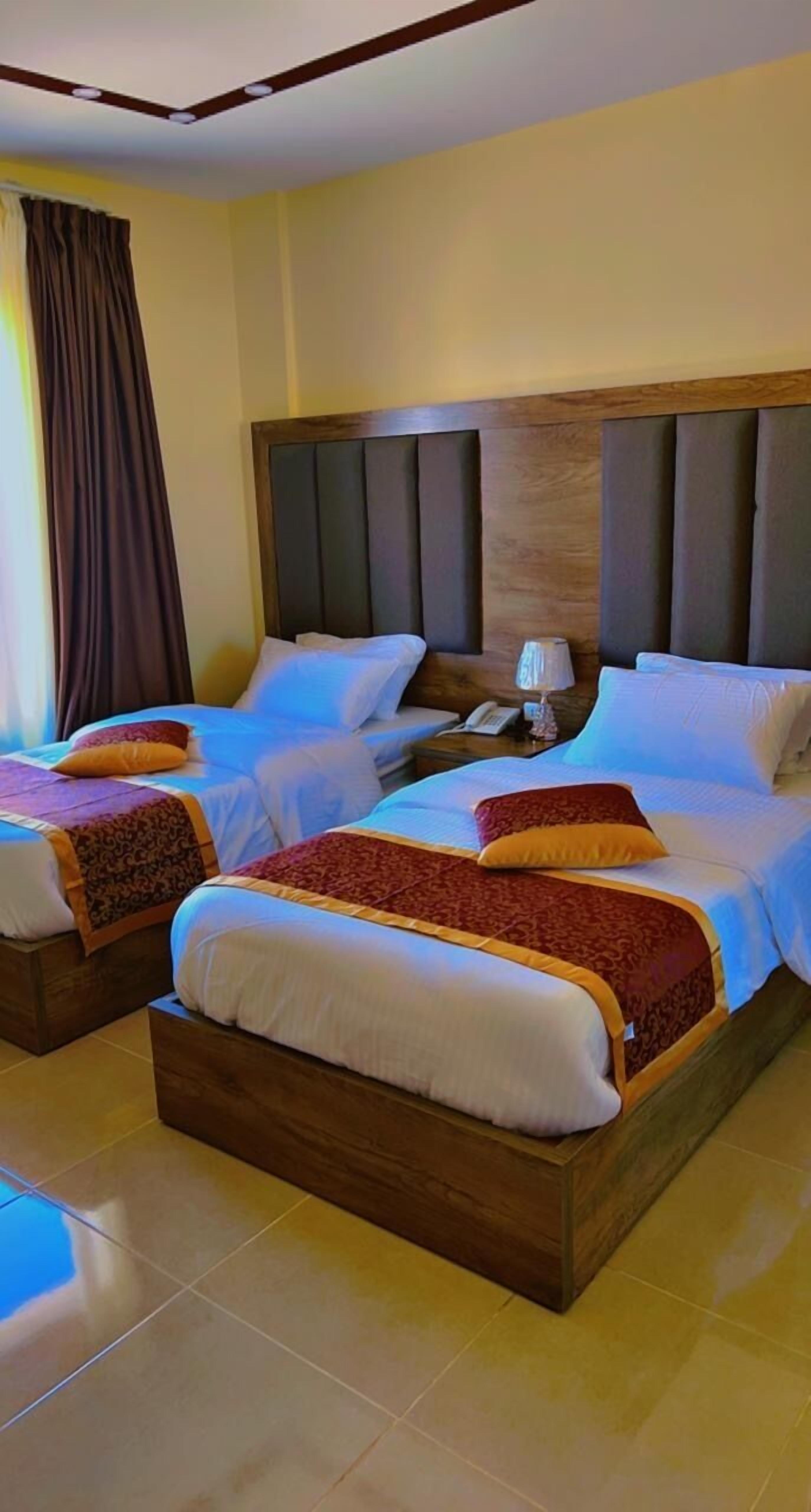 Een hotelkamer met twee bedden, houten hoofdborden en een nachtkastje met een lamp.