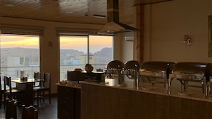 A restaurant with a view of the cityscape at sunset, featuring a bar area with grills and a dining area with tables and chairs. - Shaqilath Hotel (Wadi Musa)