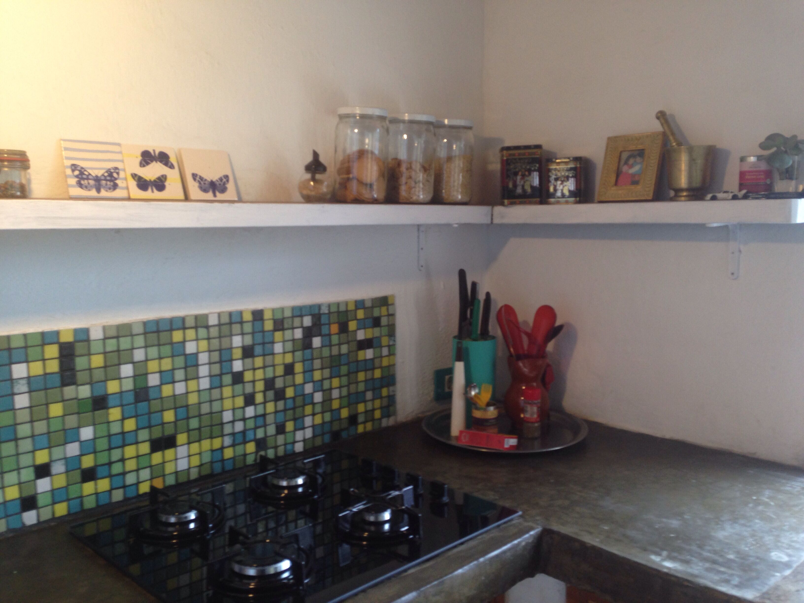 A kitchen with a mosaic backsplash, a gas stove, shelves with jars and kitchen utensils.