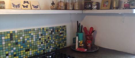 A kitchen with a mosaic backsplash, a gas stove, shelves with jars and kitchen utensils.