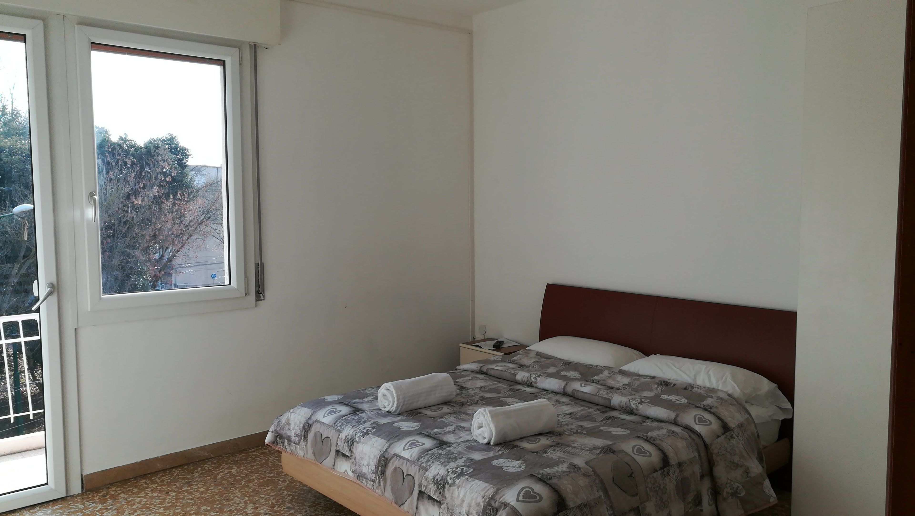 A bedroom with a bed, a nightstand, and a window.