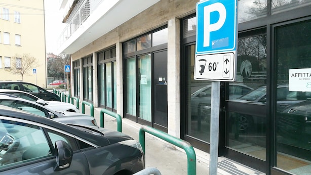 A parking lot with cars parked in front of a building with large windows and a sign indicating parking availability. - STAY VENICE GUESTHOUSE (Mestre)
