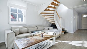 A modern living room with a wooden staircase, a white sofa, and a coffee table. - Living under thatch in Seasons - fireplace & sauna  (Groß Schwansee)