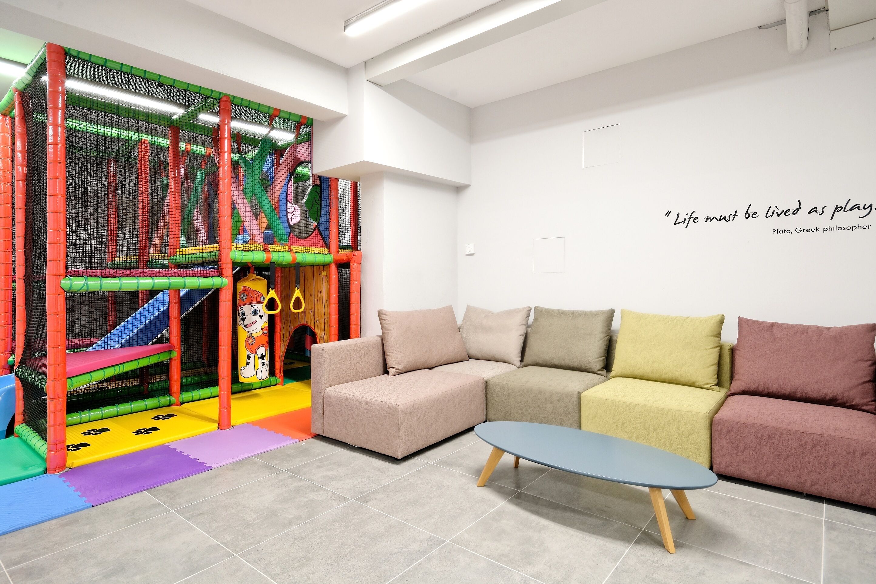 A play area with a soft play structure and a sofa set in a room with a motivational quote on the wall.
