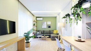 Una sala de estar moderna con sofá, mesa de centro y televisor. Hay plantas y obras de arte en las paredes.