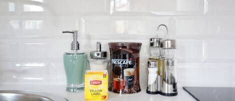 Un piano di lavoro in cucina con una macchina da caffè Nescafe Classic, una bustina di tè Lipton Yellow Label, un bicchiere d'acqua e un lavello in acciaio inossidabile.
