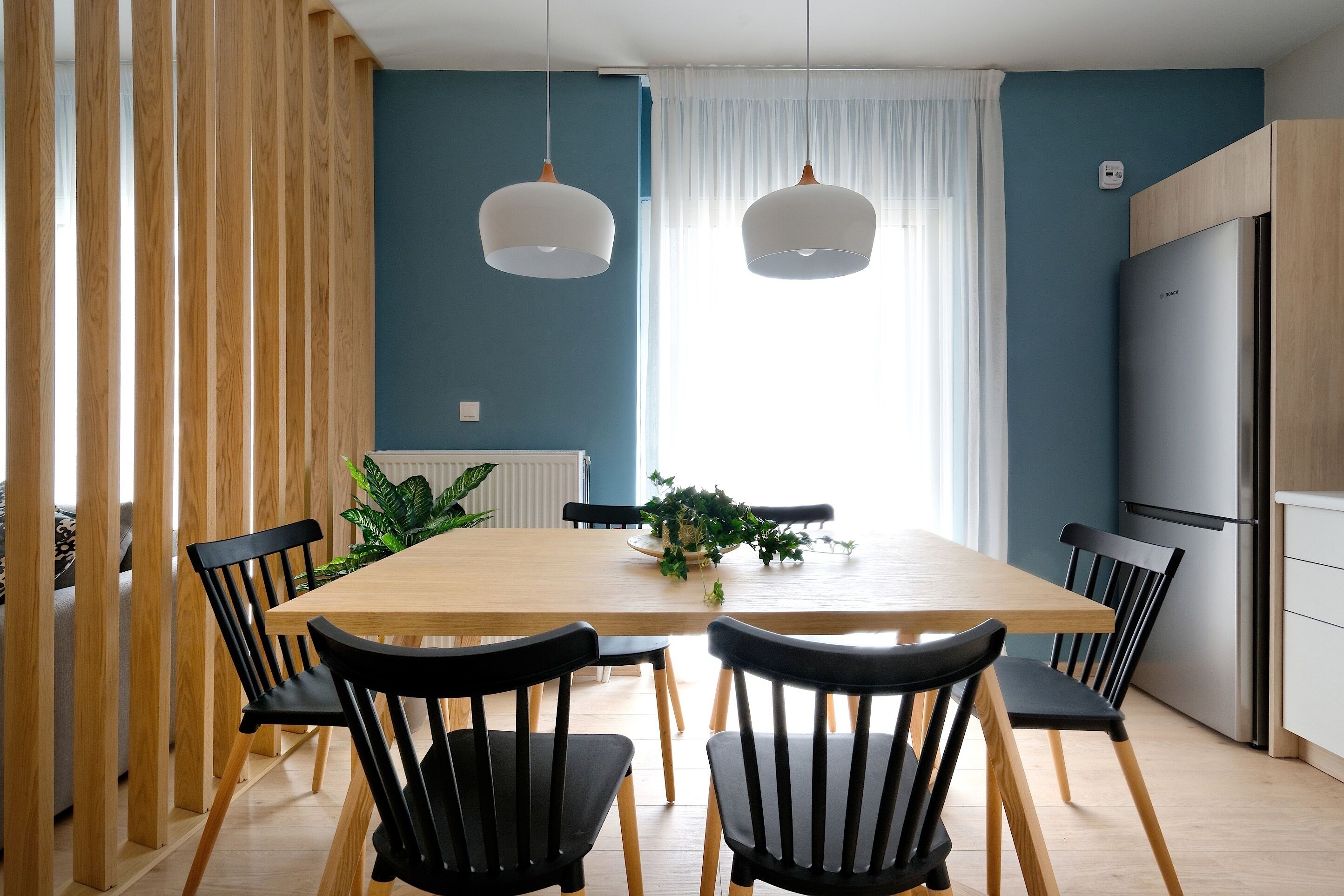 A modern kitchen with a wooden table, black chairs, and a built-in refrigerator.