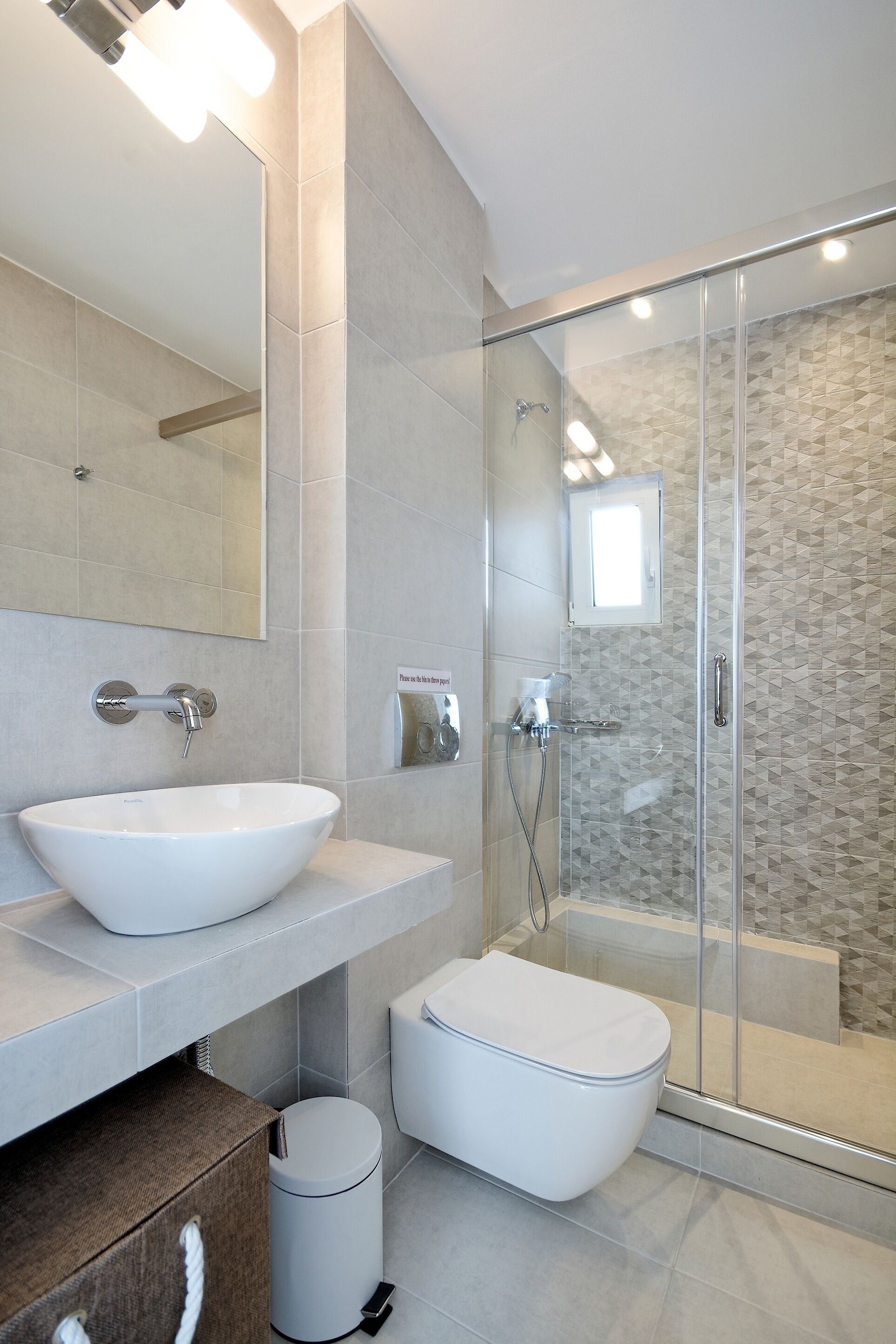 A modern bathroom with a large white sink, a glass-enclosed shower, and a toilet.